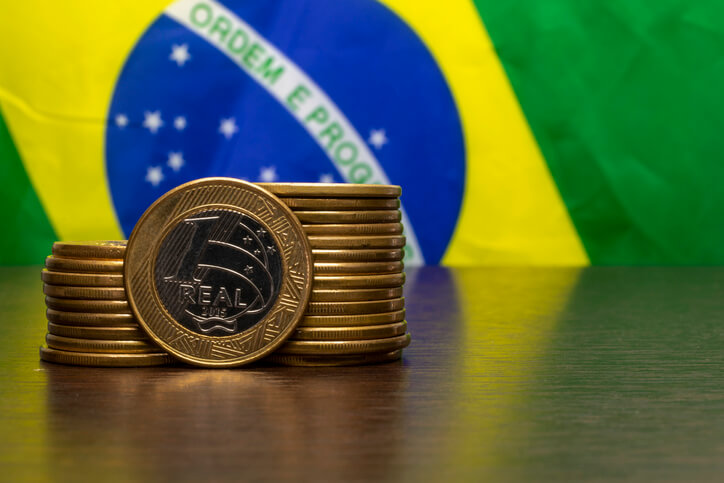 Moedas empilhadas com bandeira do Brasil ao fundo