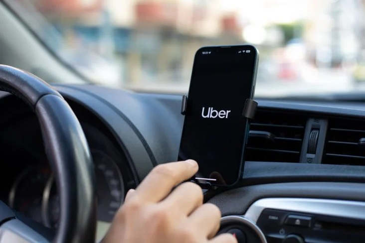 mao-de-pessoa-boa-clicando-em-celular-acom-logotipo-da-uber-afixado-em-painel-de-carro
